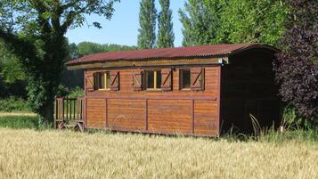 A wooden building with a red roof, surrounded by tall grass and trees.