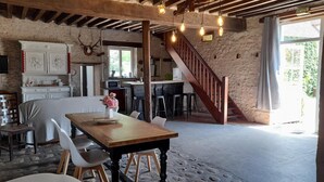 A rustic interior with a wooden dining table, white chairs, a kitchen area, and a staircase. - Roulotte à la Ferme de l'Isle (Avaray)