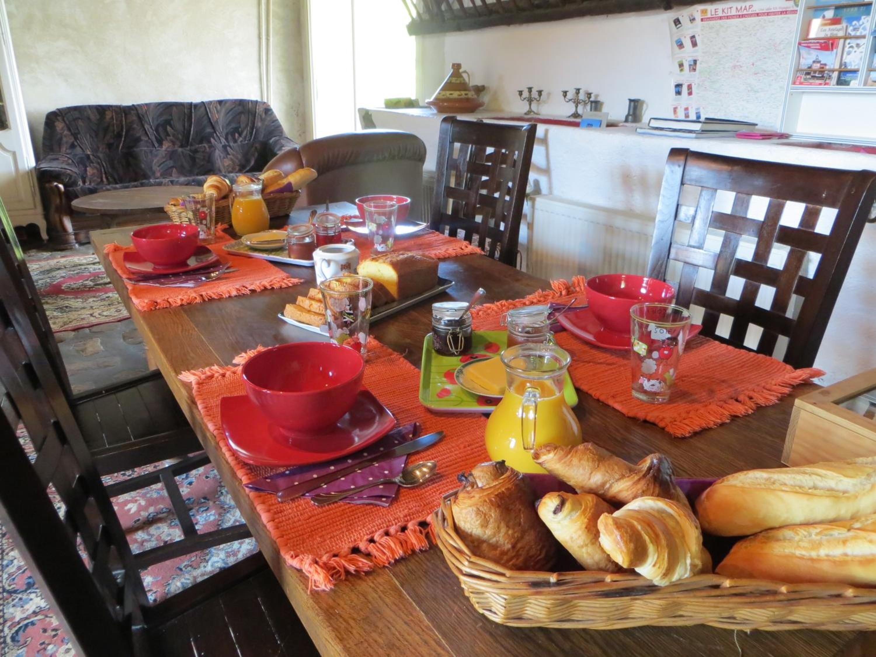 Une table à manger dressée avec des bols et des assiettes rouges, ainsi qu’un panier de pain.