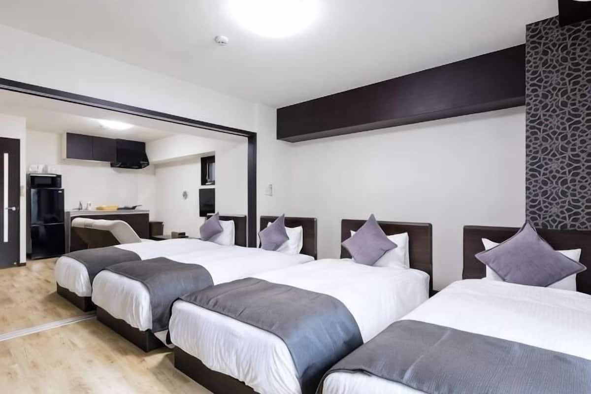 Ett hotellrum med tre sÀngar, ett litet kök och en spegel.
