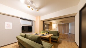 A modern living room with a wooden dining table, green sofas, and a television. - Takuto Stay Sakaisuji-Honmachi (Osaka)
