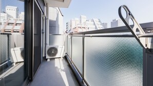 A balcony with a view of city buildings, a glass door, and an air conditioning unit. - Takuto Stay Sakaisuji-Honmachi (Osaka)