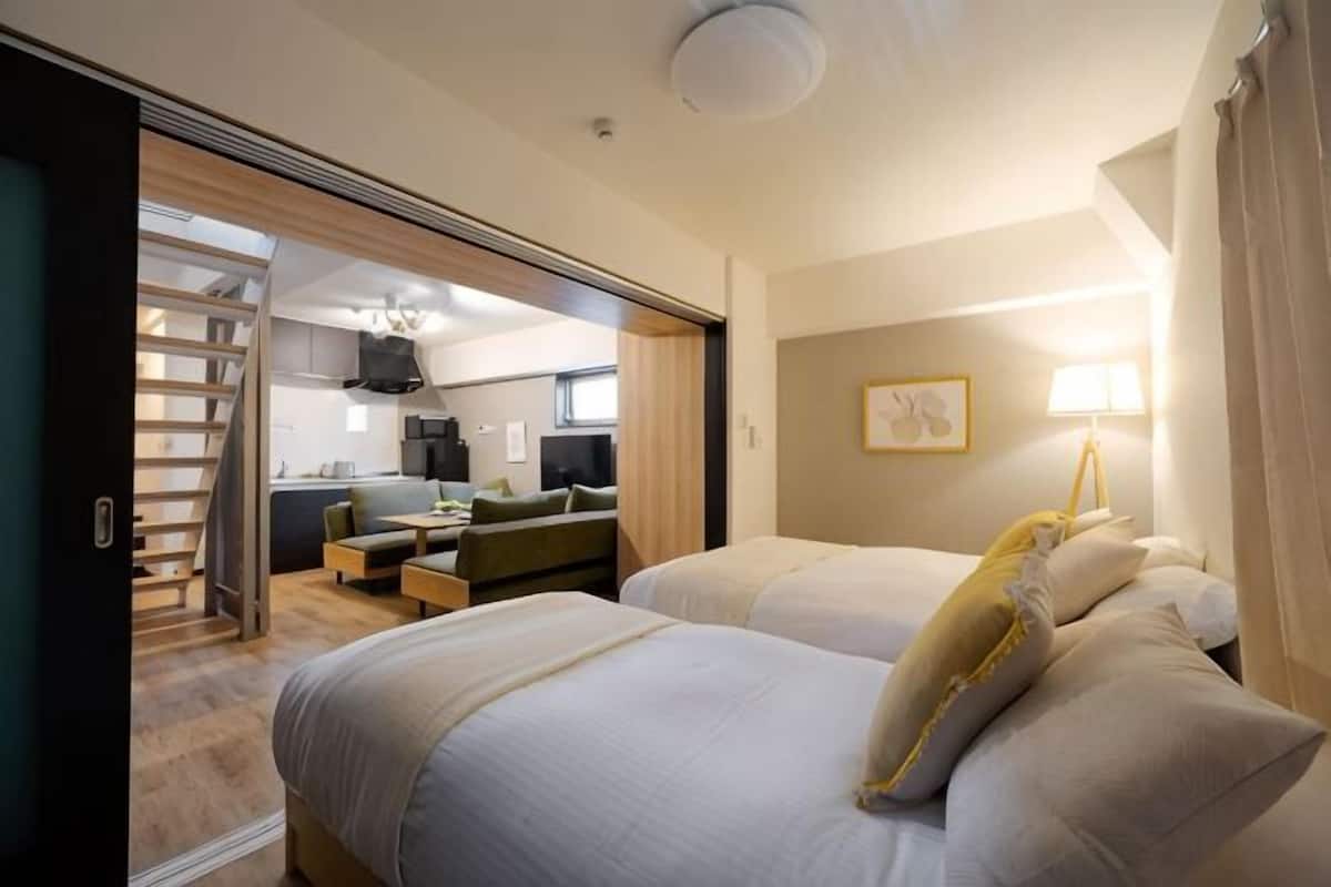 Ett hotellrum med tvÄ sÀngar, en soffa, ett matbord och ett köksutrymme som syns genom en öppen dörr.