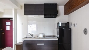 A compact kitchen with dark wood cabinets, a black microwave, and a refrigerator. - Takuto Stay Sakaisuji-Honmachi (Osaka)