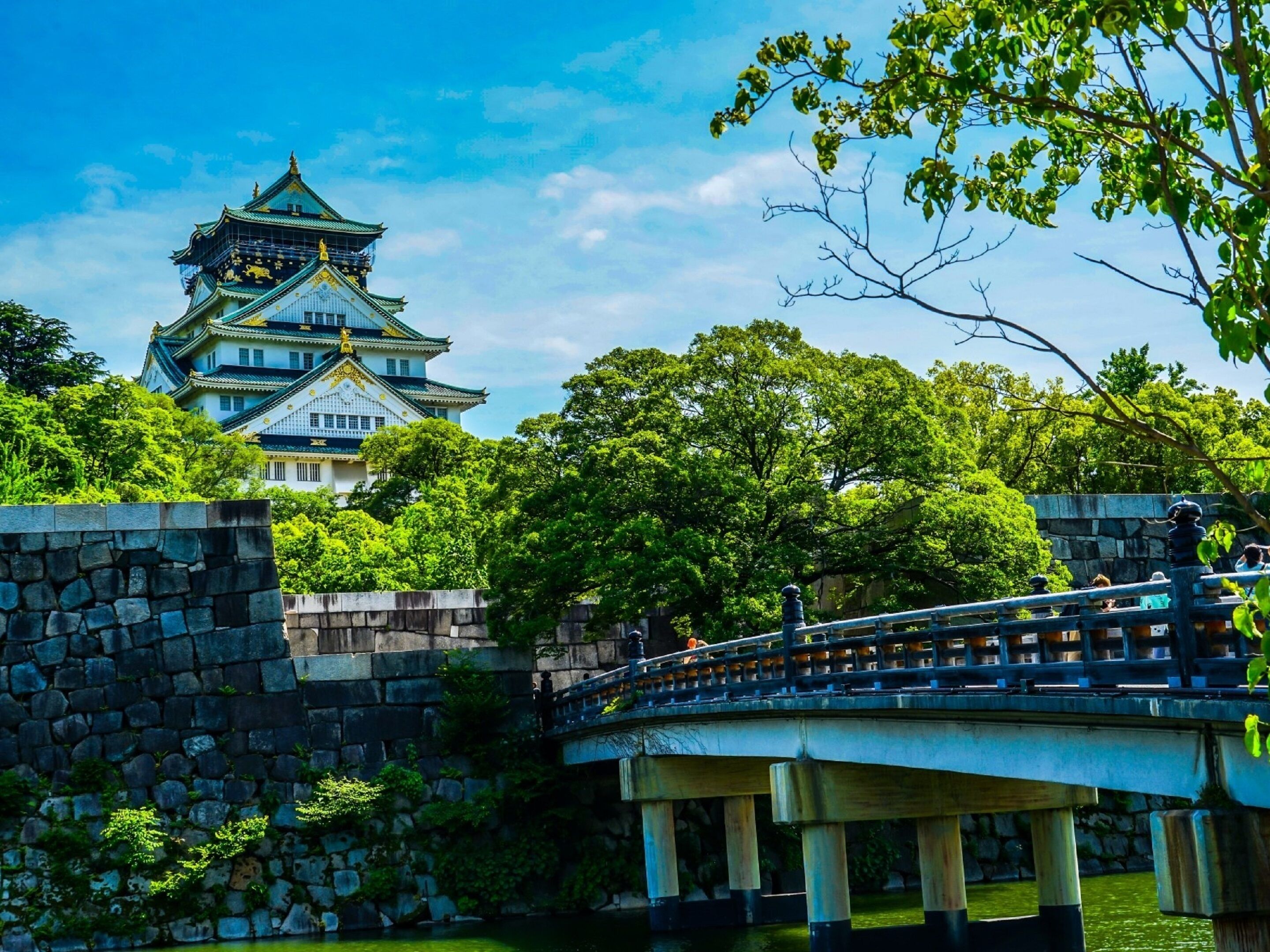Eine traditionelle japanische Burg mit mehrstufiger Dachkonstruktion, einer Steinmauer und einer Brücke mit Geländern.