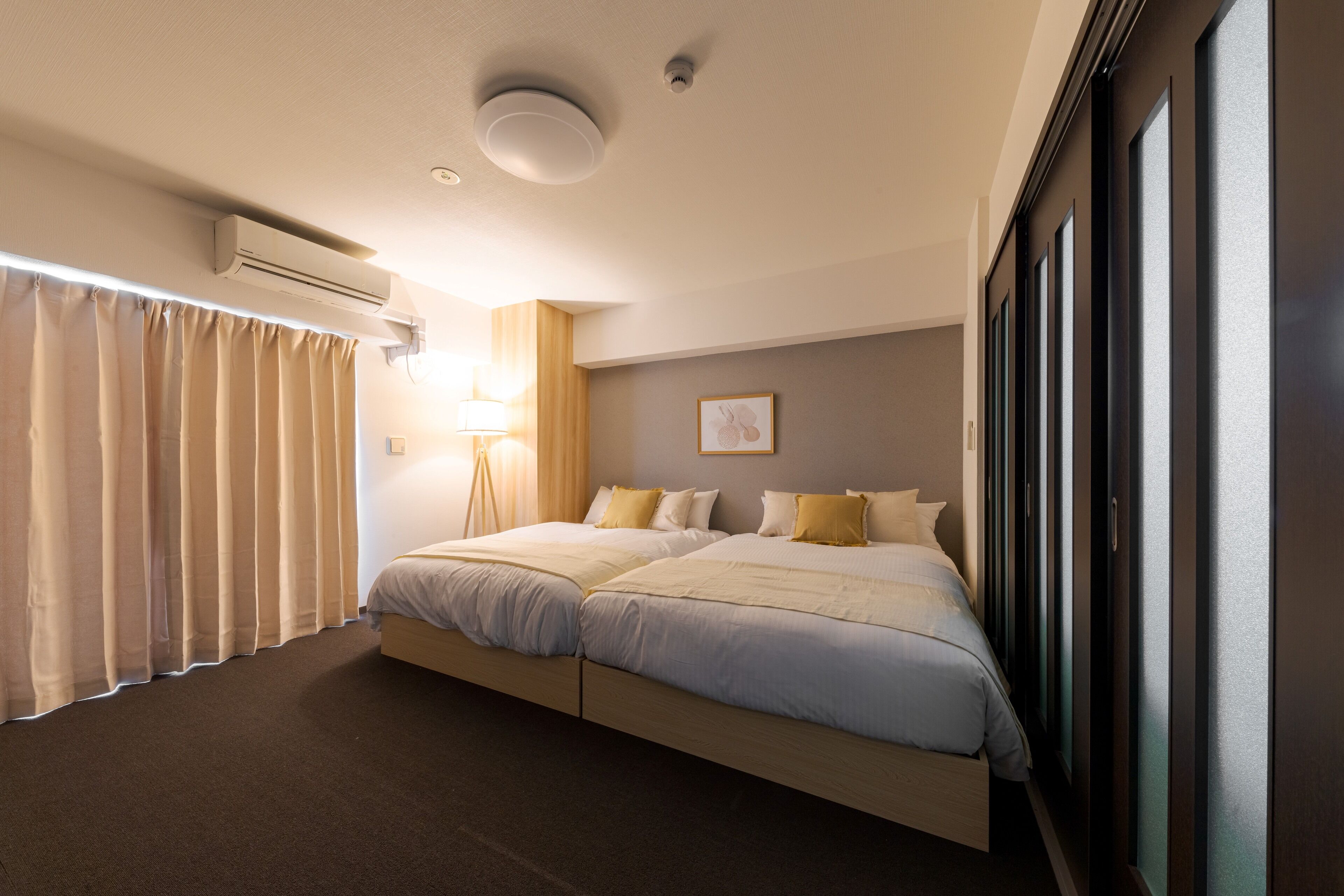 A hotel room with a large bed, a bedside table, a lamp, and a window with curtains.