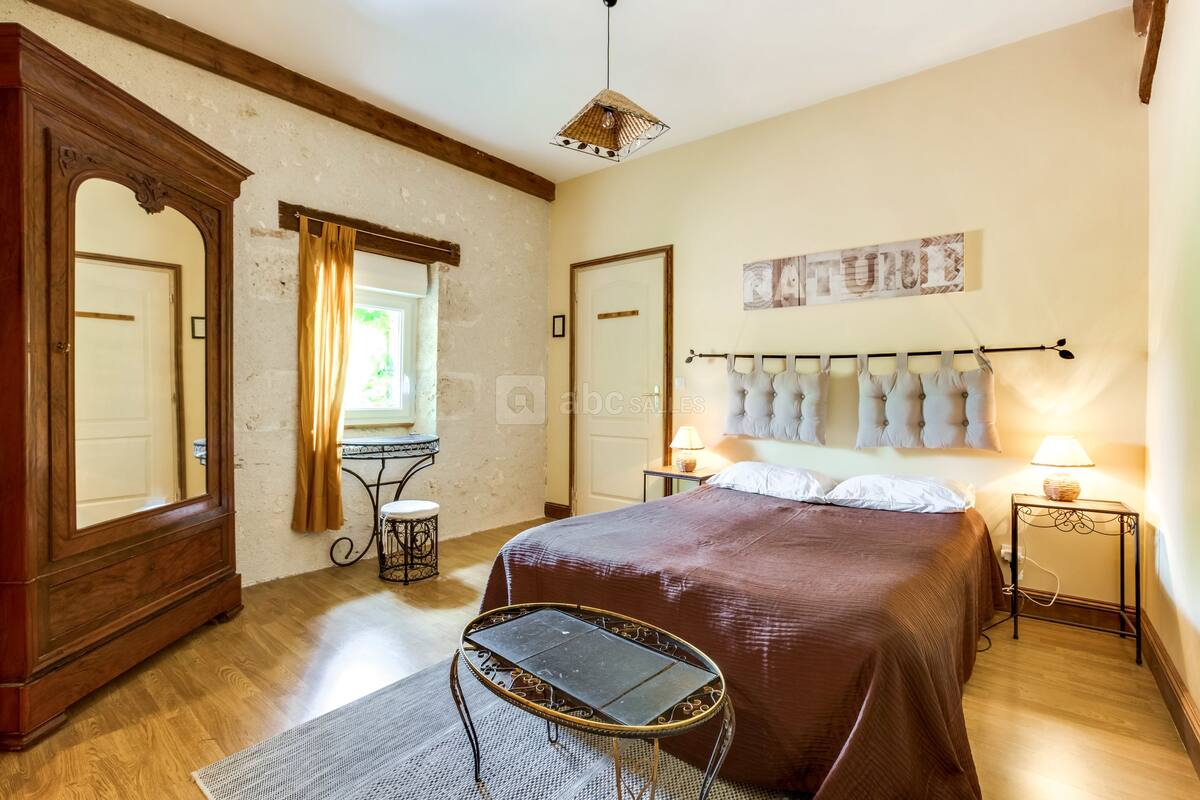 Une chambre avec un grand lit, une armoire en bois, une petite table et une fenêtre avec des rideaux.