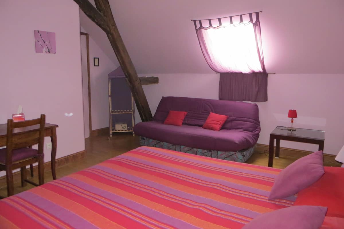 Une chambre à coucher avec un lit, une chaise, une petite table et une fenêtre avec des rideaux.