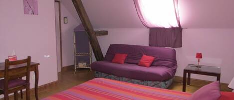 Un dormitorio con cama, una silla, una mesita y una ventana con cortinas.
