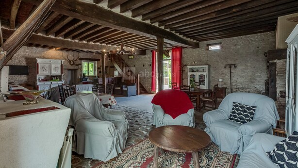 A rustic interior with exposed wooden beams, a stone wall, and a cozy seating area with a patterned rug. - Chambres d'hotes Domaine de l'Isle (Avaray)