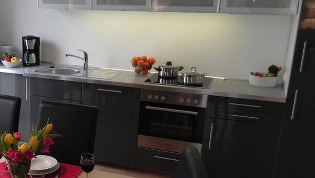 A modern kitchen with a sink, stove, oven, and cabinets. There is a coffee maker, a bowl of fruit, and a vase with flowers on the counter.