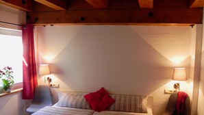 A bedroom with two beds, a window with a curtain, a chair, and two wall-mounted lamps.