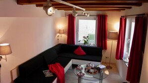 A modern living room with a black sofa, a glass coffee table, and red curtains.