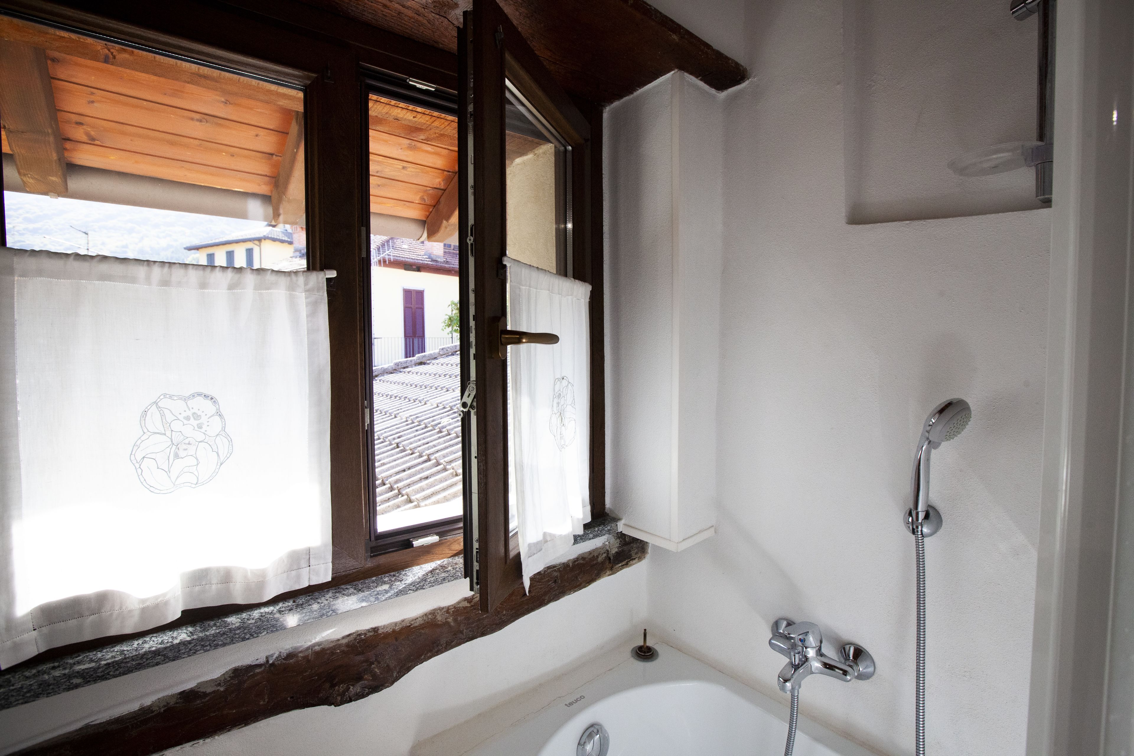 A bathroom with a bathtub, a shower, and a window with curtains.