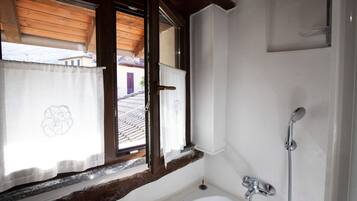 A bathroom with a bathtub, a shower, and a window with curtains.