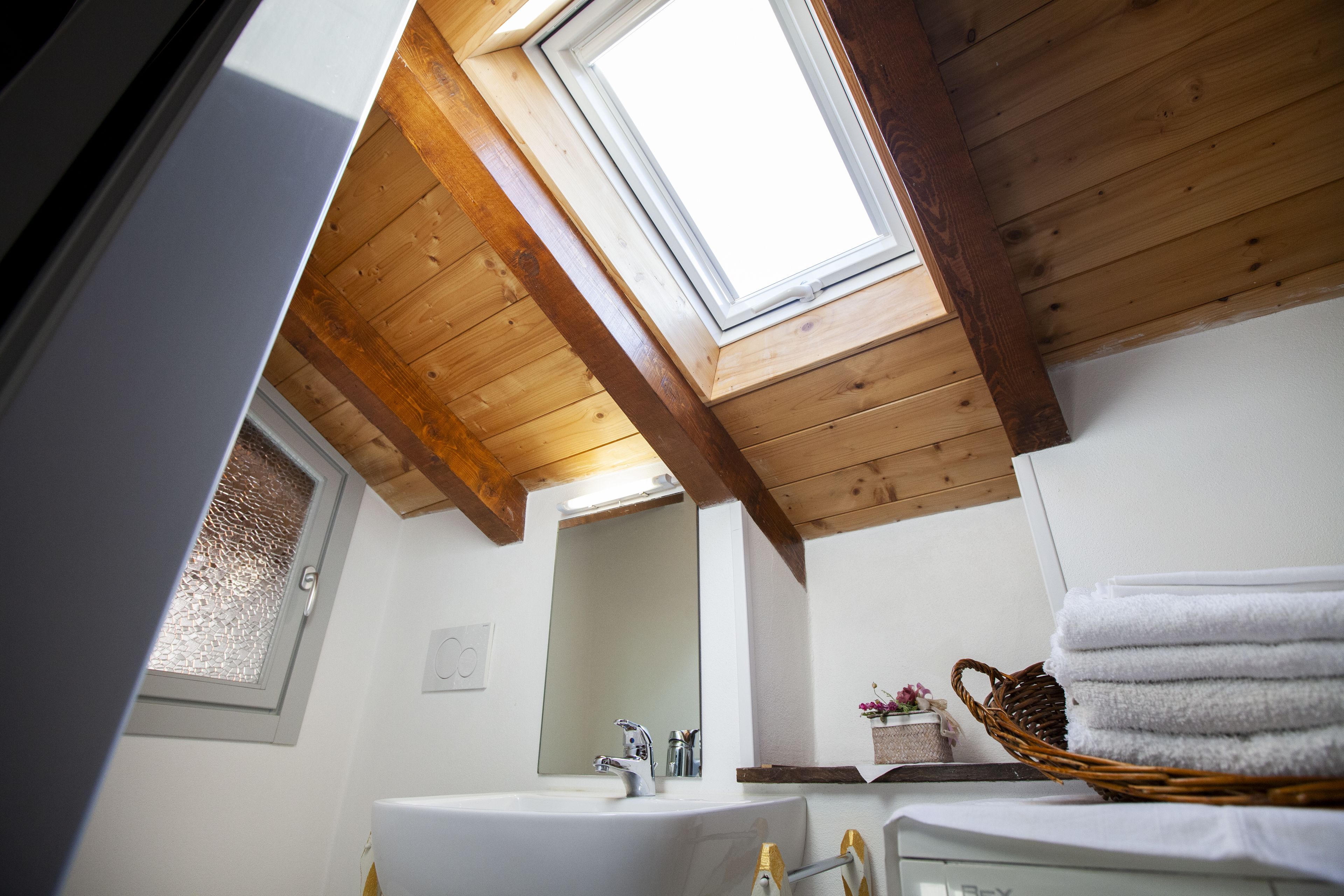 Un baño con tragaluz, vigas de madera en el techo y una canasta de toallas.