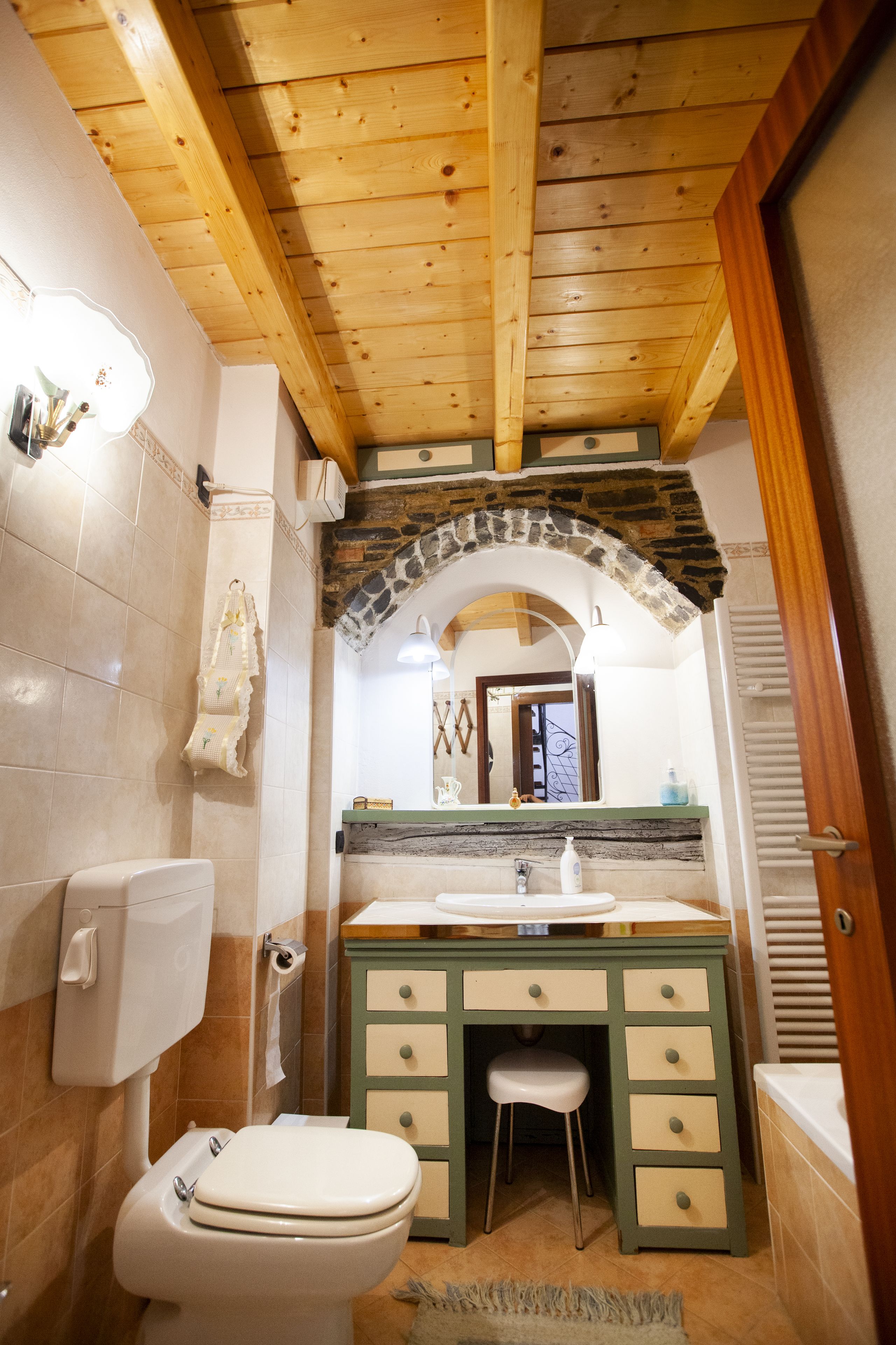 Casa de banho com teto de madeira, arco de pedra, lavatório, sanita e espelho.