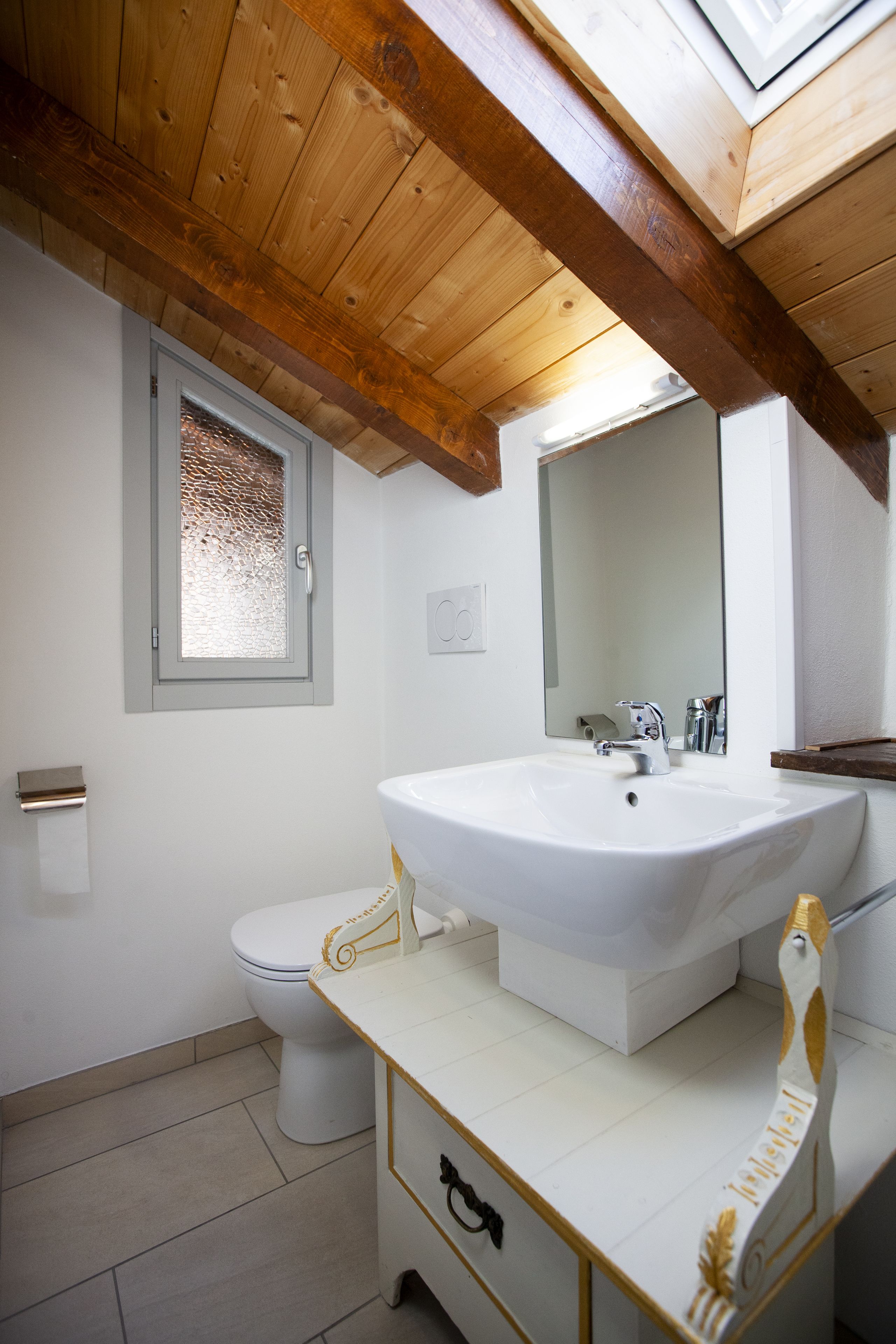 Un baño con lavamanos blanco, espejo, ventana y retrete.