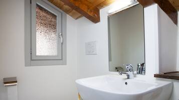 Un baño con lavamanos blanco, espejo, ventana y retrete.