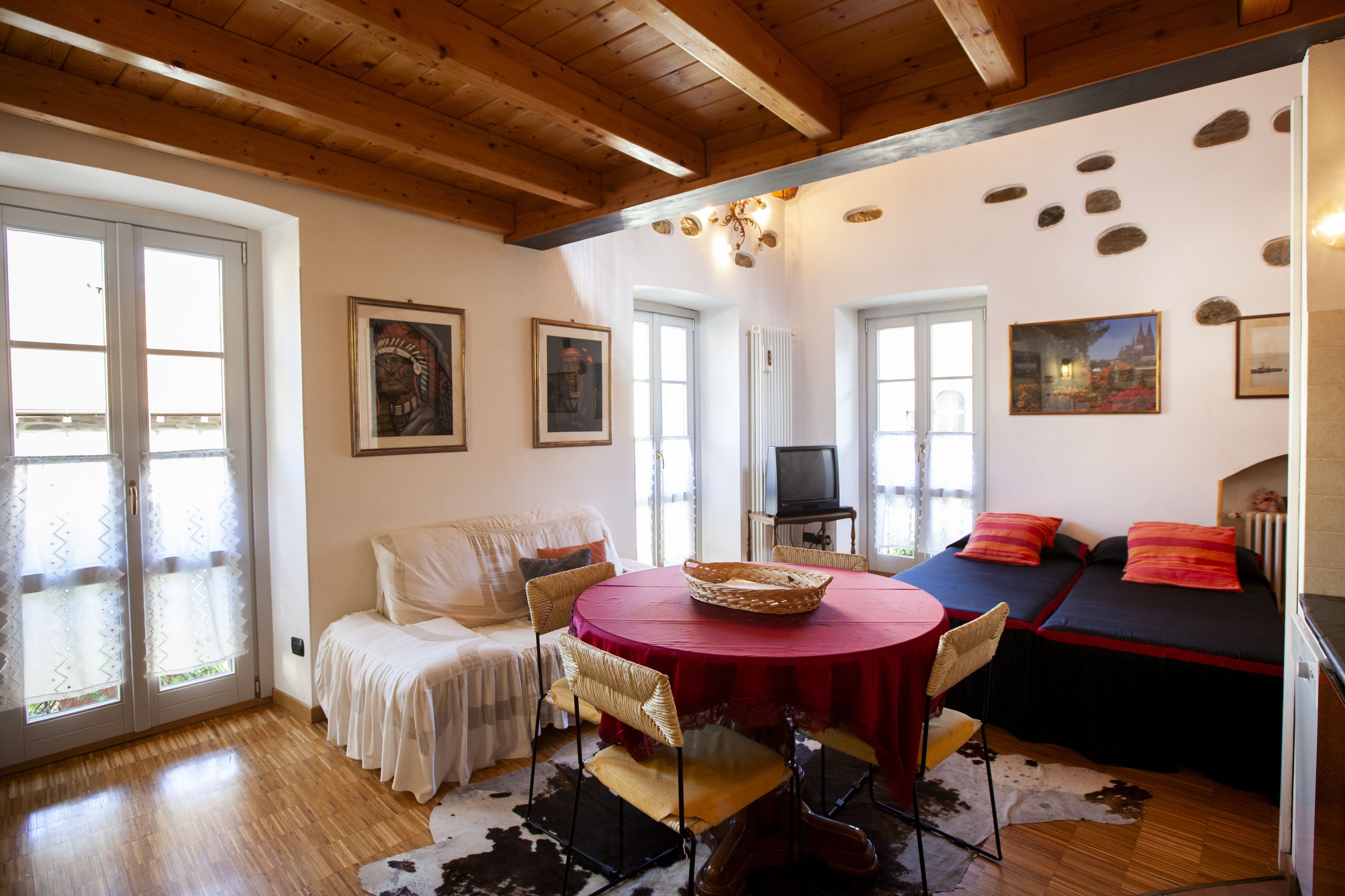 Una habitación acogedora con techo de madera, una mesa redonda con sillas, un sofá y un televisor.