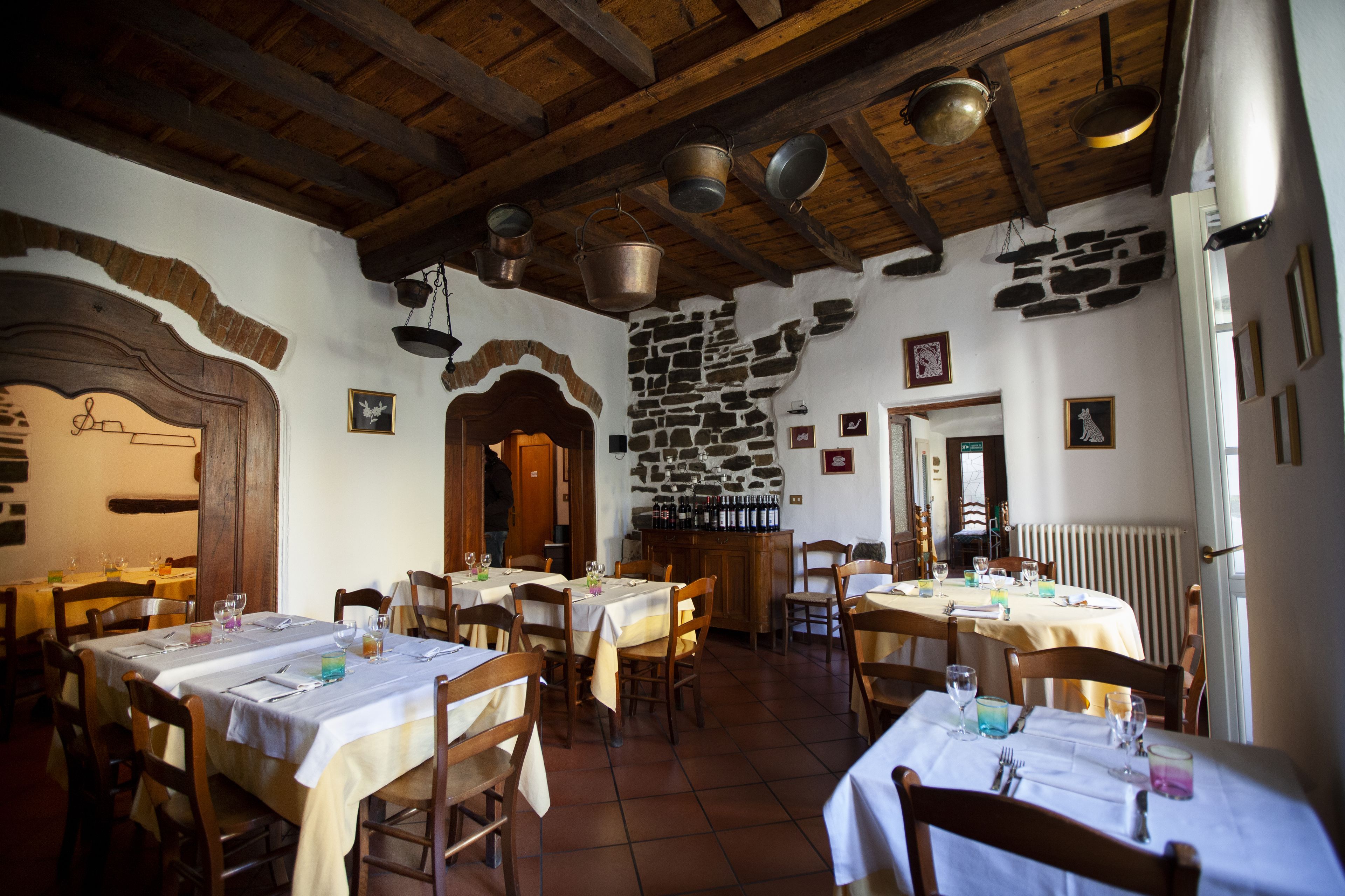 Een restaurant met houten balken en stenen muren, tafels gedekt met witte tafellinnen en stoelen.