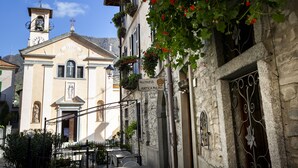 A building with a bell tower, a sign reading "Hostaria Antica Molina", and outdoor seating with tables and chairs. - Antica Molina (Faggeto Lario)