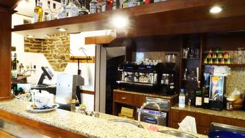 Uma área de bar com máquina de café, prateleiras de garrafas de bebidas e uma parede de pedra ao fundo.
