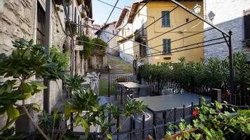 Una calle estrecha flanqueada por edificios, con mesas al aire libre y una escalera que sube a un nivel superior.