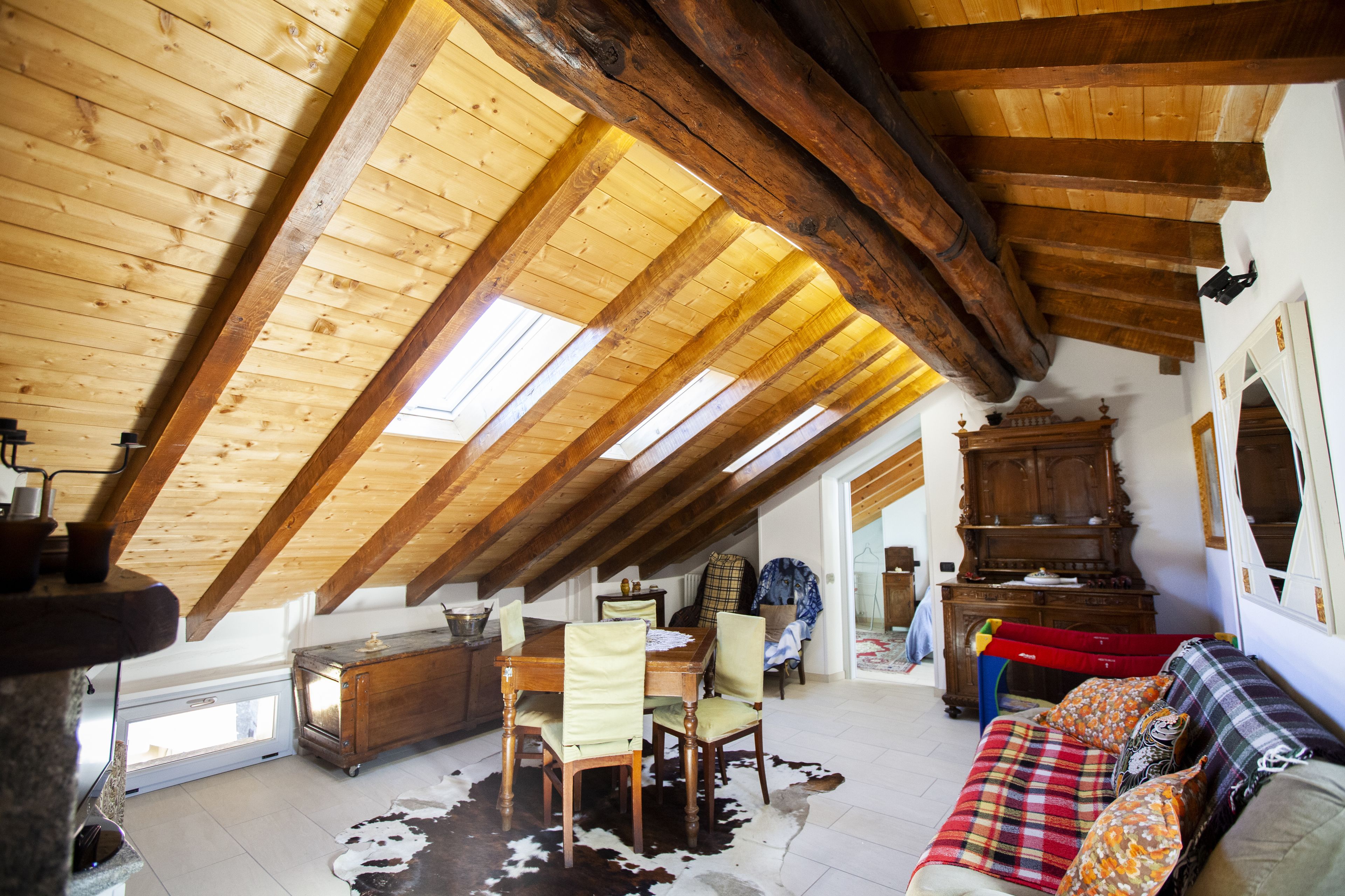 Een zolderkamer met hoge plafonds, houten balken, een eettafel met stoelen, een bank en een kleden van koeienhuid.
