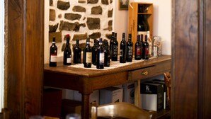 A wooden wine rack with bottles, a stone wall, and a wooden table with glasses. - Antica Molina (Faggeto Lario)
