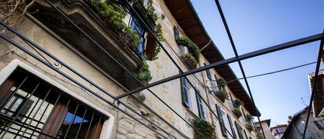 Una stretta via con edifici in pietra, balconi fioriti e una insegna che indica un ristorante.