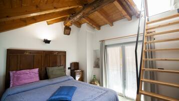 A bedroom with a wooden ceiling, a bed with a blue pillow, a wooden ladder, and a window with curtains.