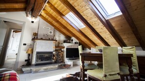 A cozy attic room with a fireplace, wooden beams, a television, and a dining table. - Antica Molina (Faggeto Lario)