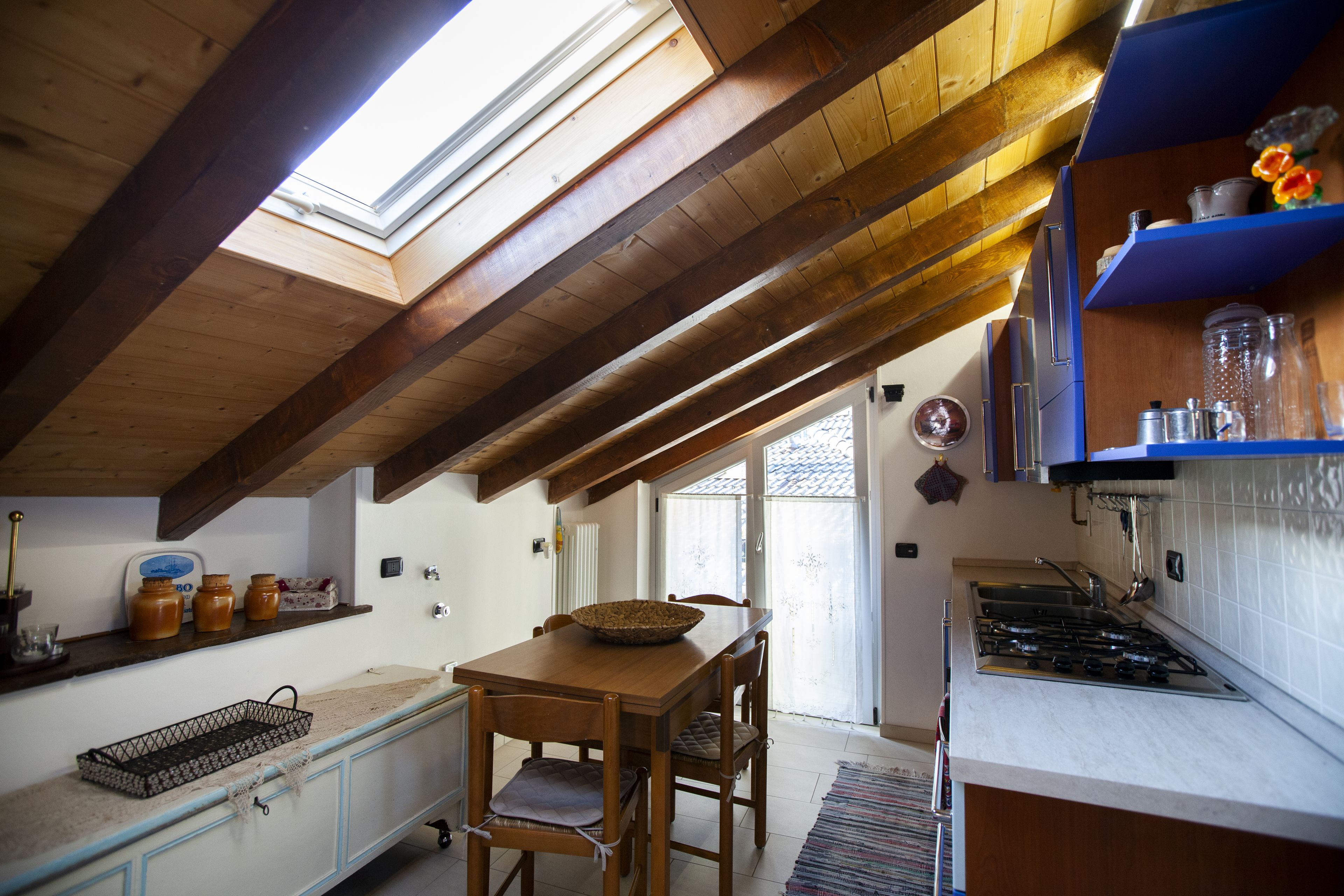 A kitchen with a skylight, wooden beams, a dining table, chairs, and a stove.