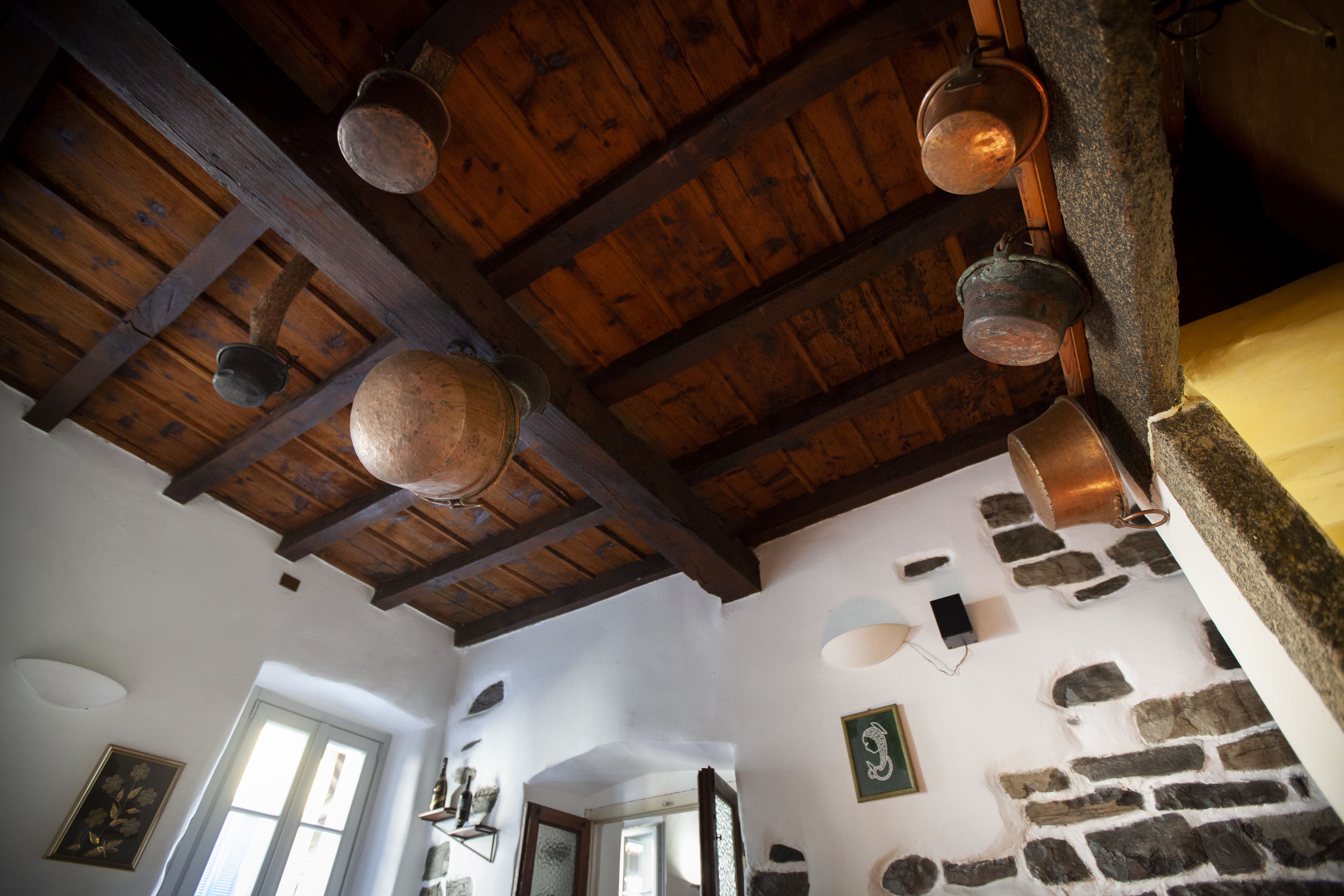 Un intérieur rustique avec des poutres apparentes, des murs en pierre et des casseroles en cuivre suspendues.