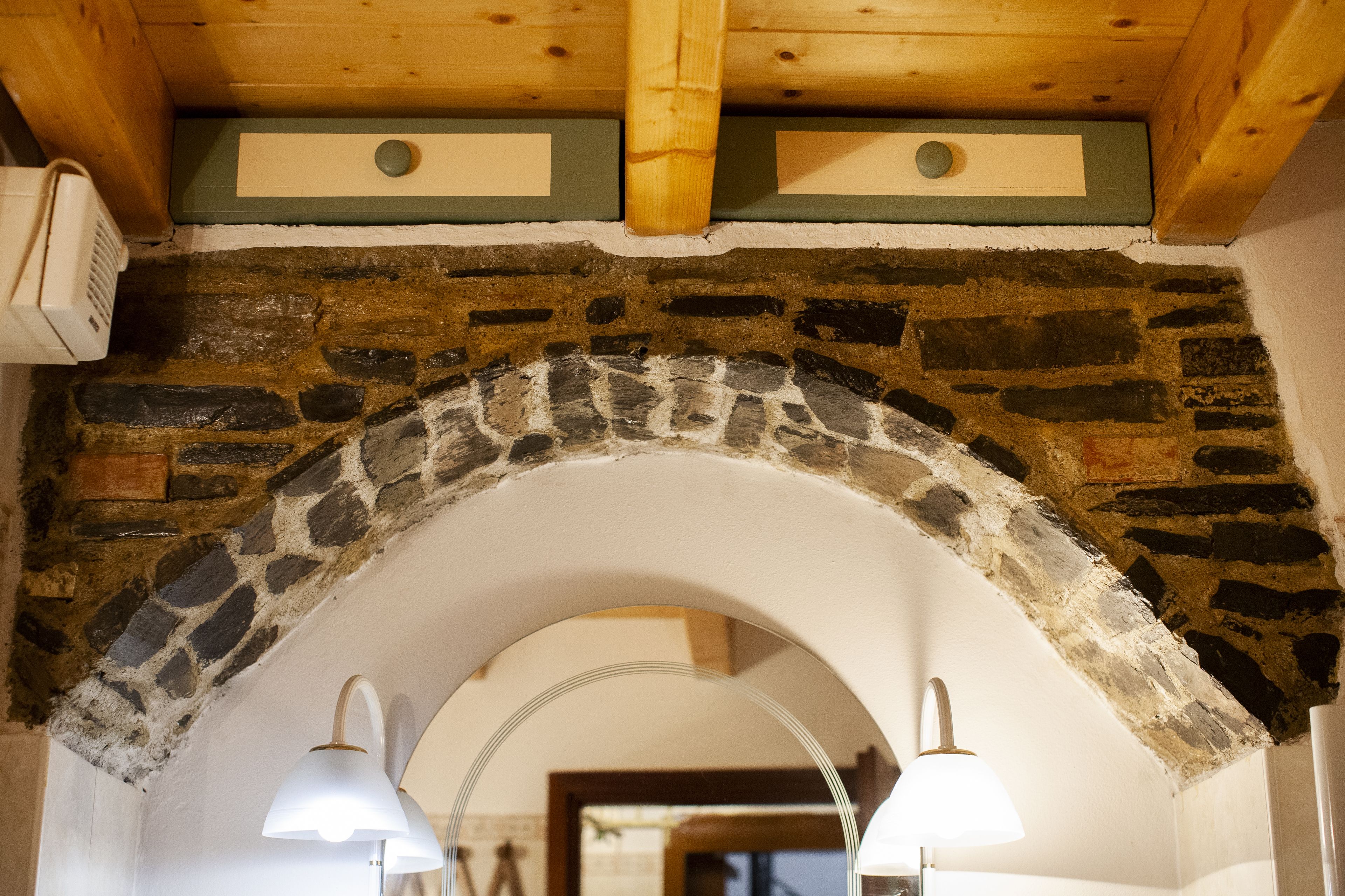 Un arco de piedra con techo de madera y dos lámparas fijadas a la pared.