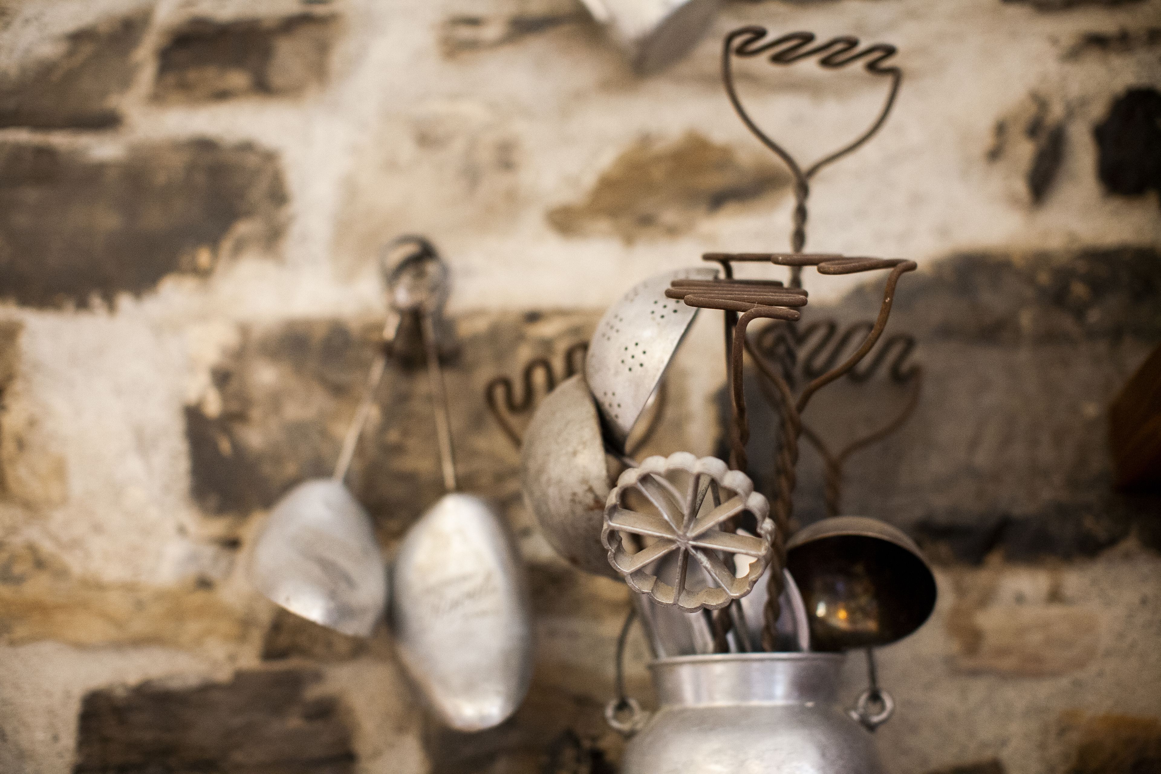 A metal pot with a lid and a spoon hanging on a rustic brick wall.