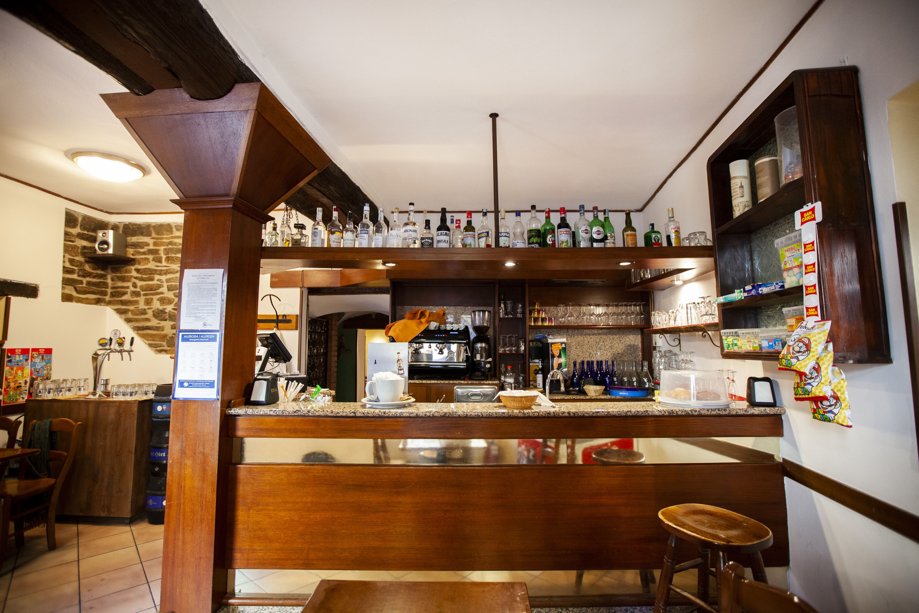 A bar area with a counter, stools, and shelves stocked with bottles and glasses.