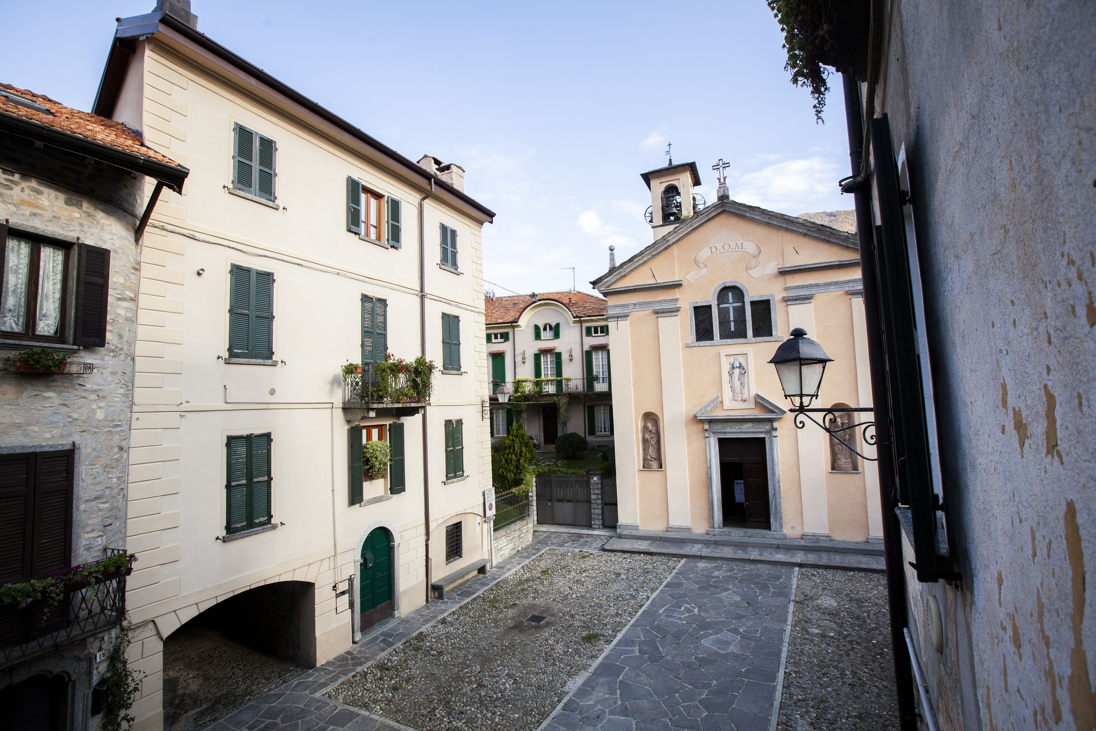A narrow cobblestone street between buildings with stone facades and green shutters.
