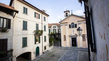 A narrow cobblestone street between buildings with stone facades and green shutters.
