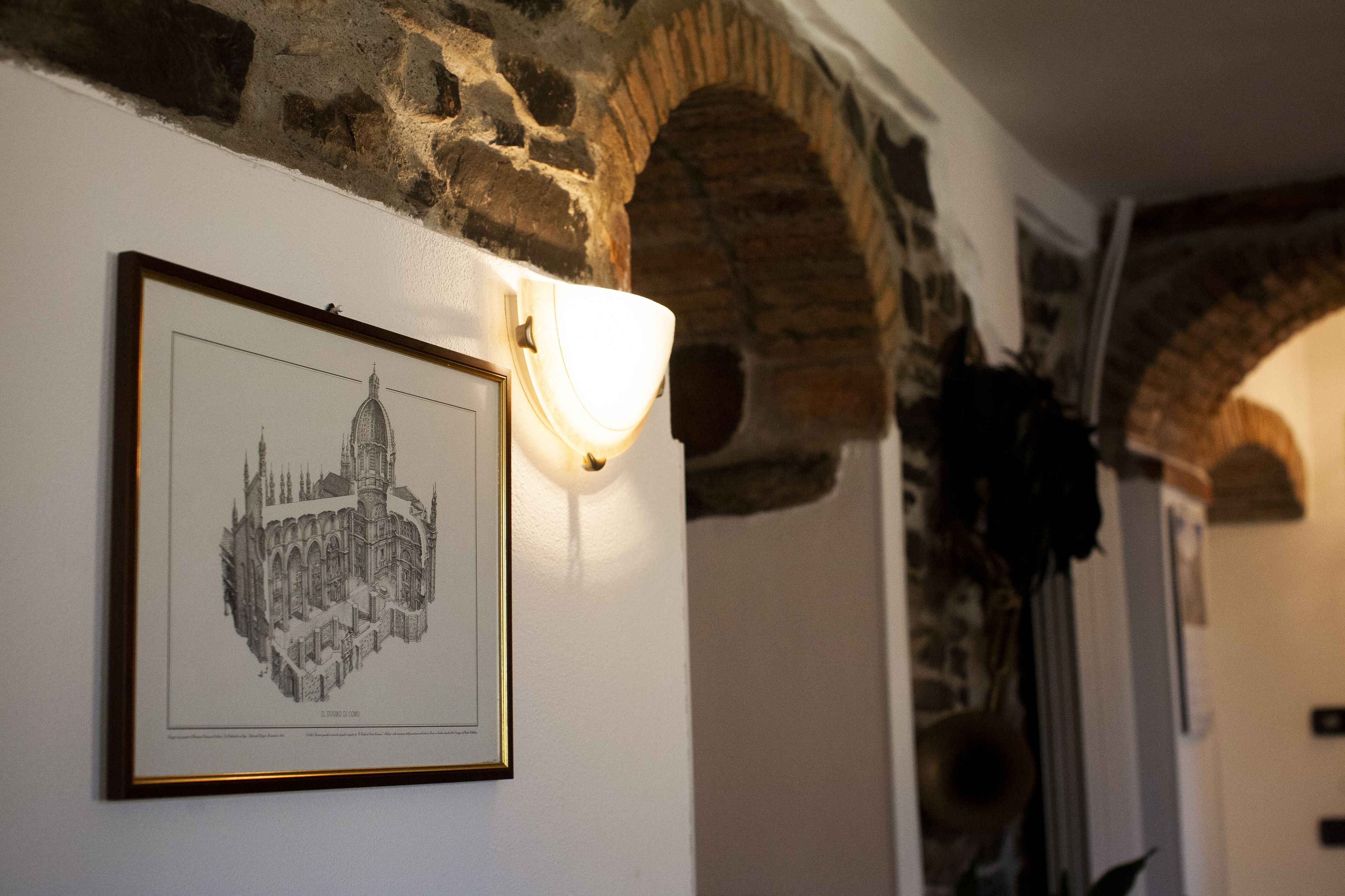 A framed architectural drawing on a wall, a stone archway, and a wall-mounted light fixture.