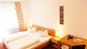 Ein Hotelzimmer mit einem großen Bett, zwei Nachttischen mit Lampen, einem Holztisch, einem Stuhl und einem Mülleimer.