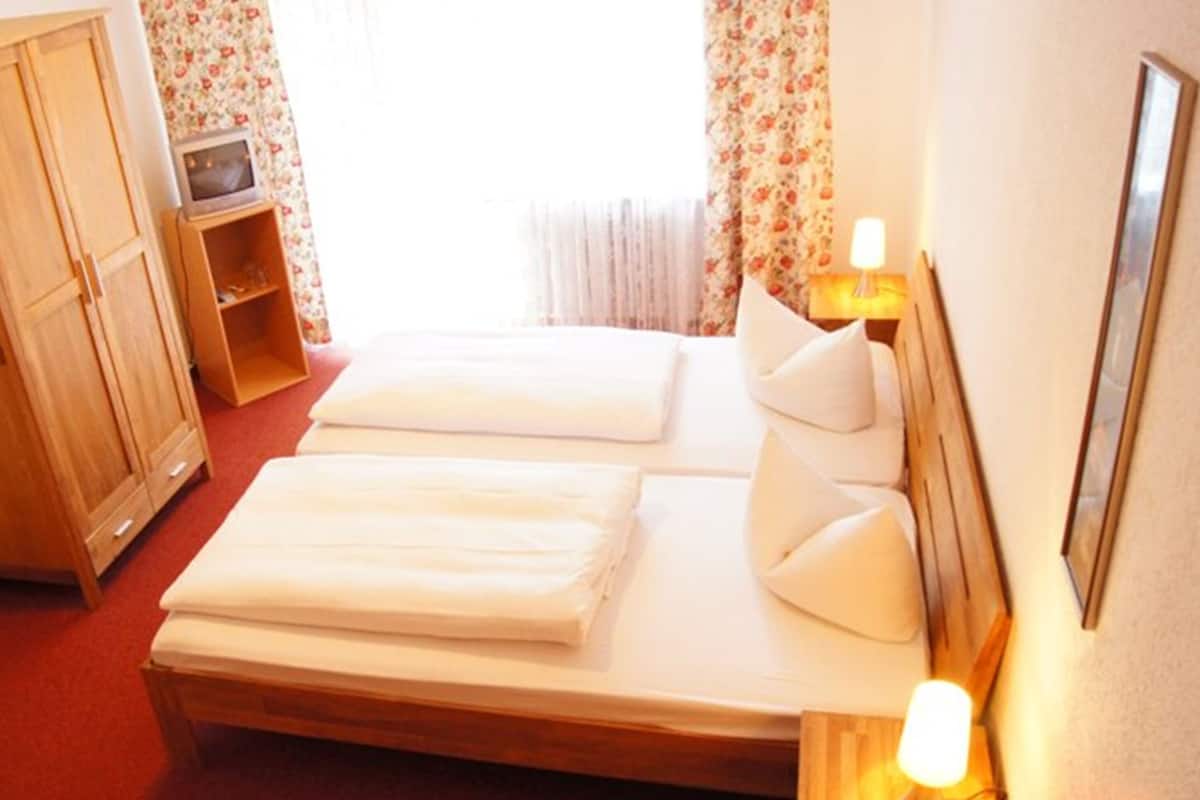 A hotel room with two beds, wooden wardrobe, and a small shelf with a television.