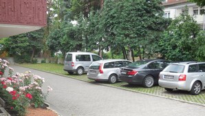 Ein Parkplatz mit mehreren in einer Reihe stehenden Autos, einem Blumenbeet mit rosa Blumen und einem Gebäude im Hintergrund.