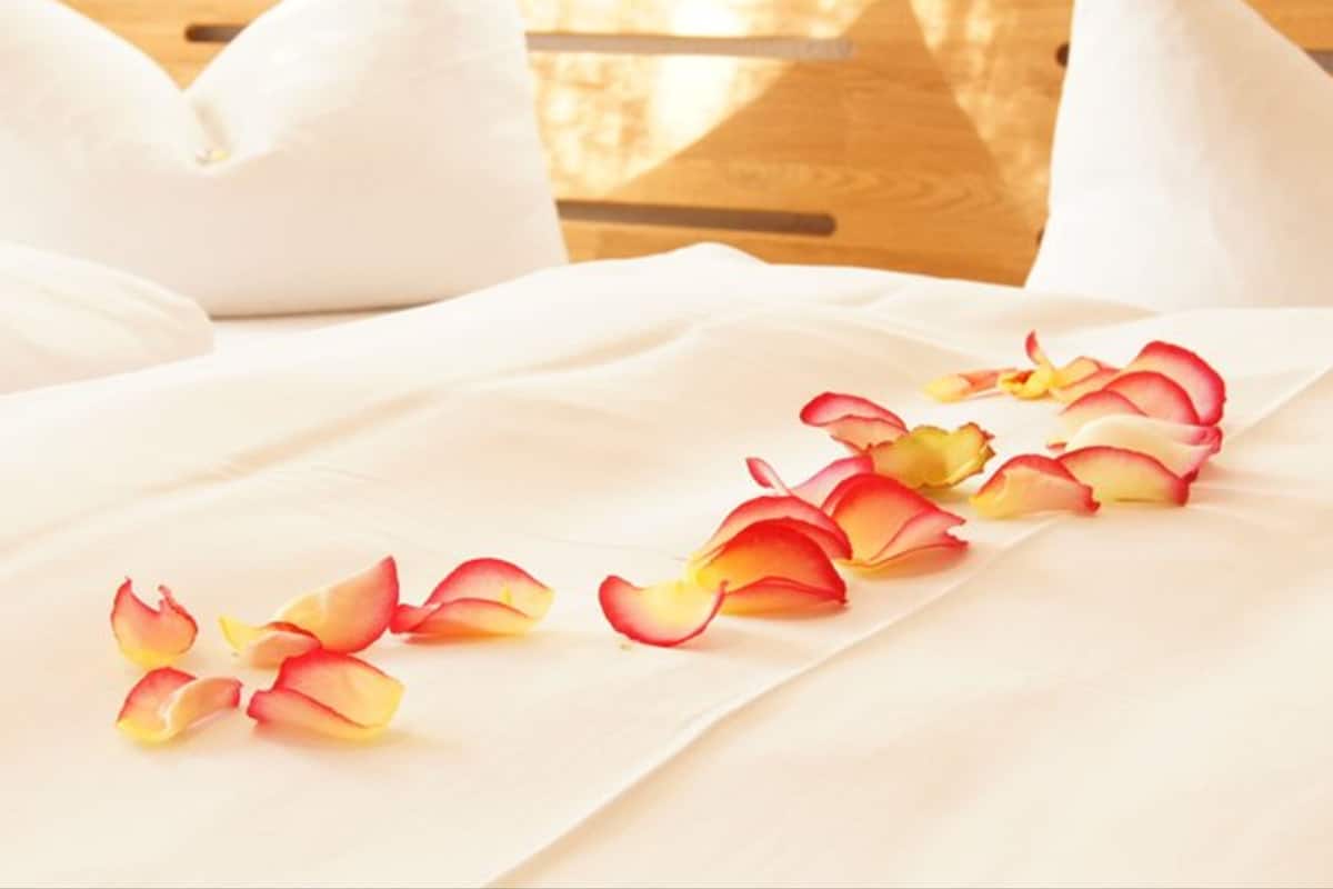 A bed with white linens and rose petals arranged on it.