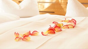 A bed with white linens and rose petals arranged on it.