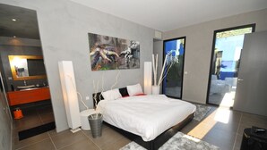 Une chambre à coucher moderne avec un grand lit, une salle de bain dotée d’un miroir et d’une armoire orange, et un tableau accroché au mur.