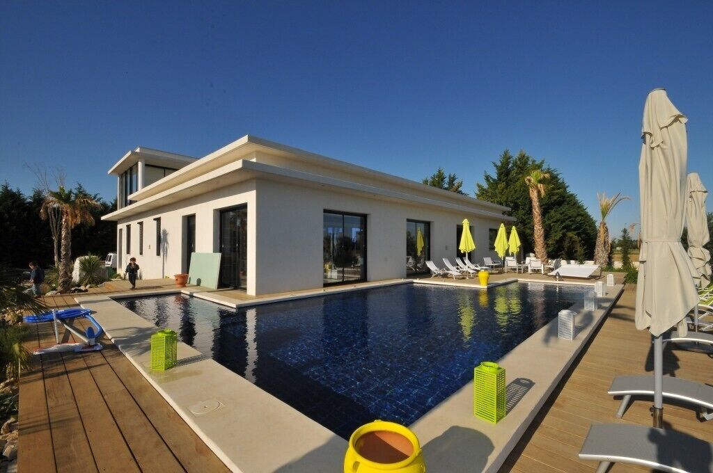 A modern poolside area with a clear blue pool, lounge chairs, and umbrellas.