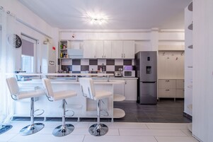 Una cocina moderna con armarios blancos, una isla central con taburetes, electrodomésticos de acero inoxidable y un salpicadero a cuadros.