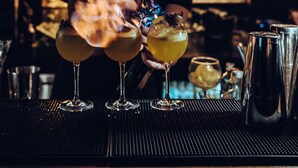 A bartender preparing drinks at a bar with a variety of bottles in the background. - Harmon House (Brussels)